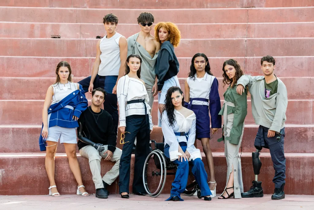 Diverse group of inclusive fashion models posing on outdoor red steps for Iulia Barton, showcasing adaptive streetwear, modern asymmetric tailoring, prosthetics, and wheelchairs.