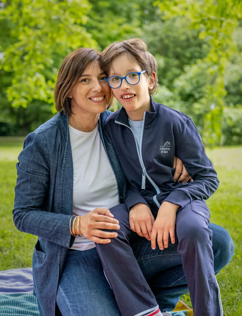 Portrait of Elisa and her son Giovanni smiling together in a park, wearing matching inclusive navy blue casual wear from the I Vestiti di Gio clothing line.