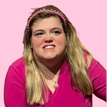 Close-up studio portrait of a blonde woman wearing a pink V-neck top, gold necklace, and a beaded pink headband against a pink backdrop.