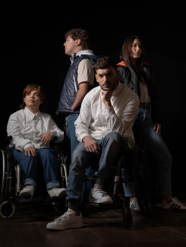 Editorial group fashion portrait of four models with disabilities posing against a dark background, featuring stylish white button-down shirts, denim jeans, and a puffer vest.